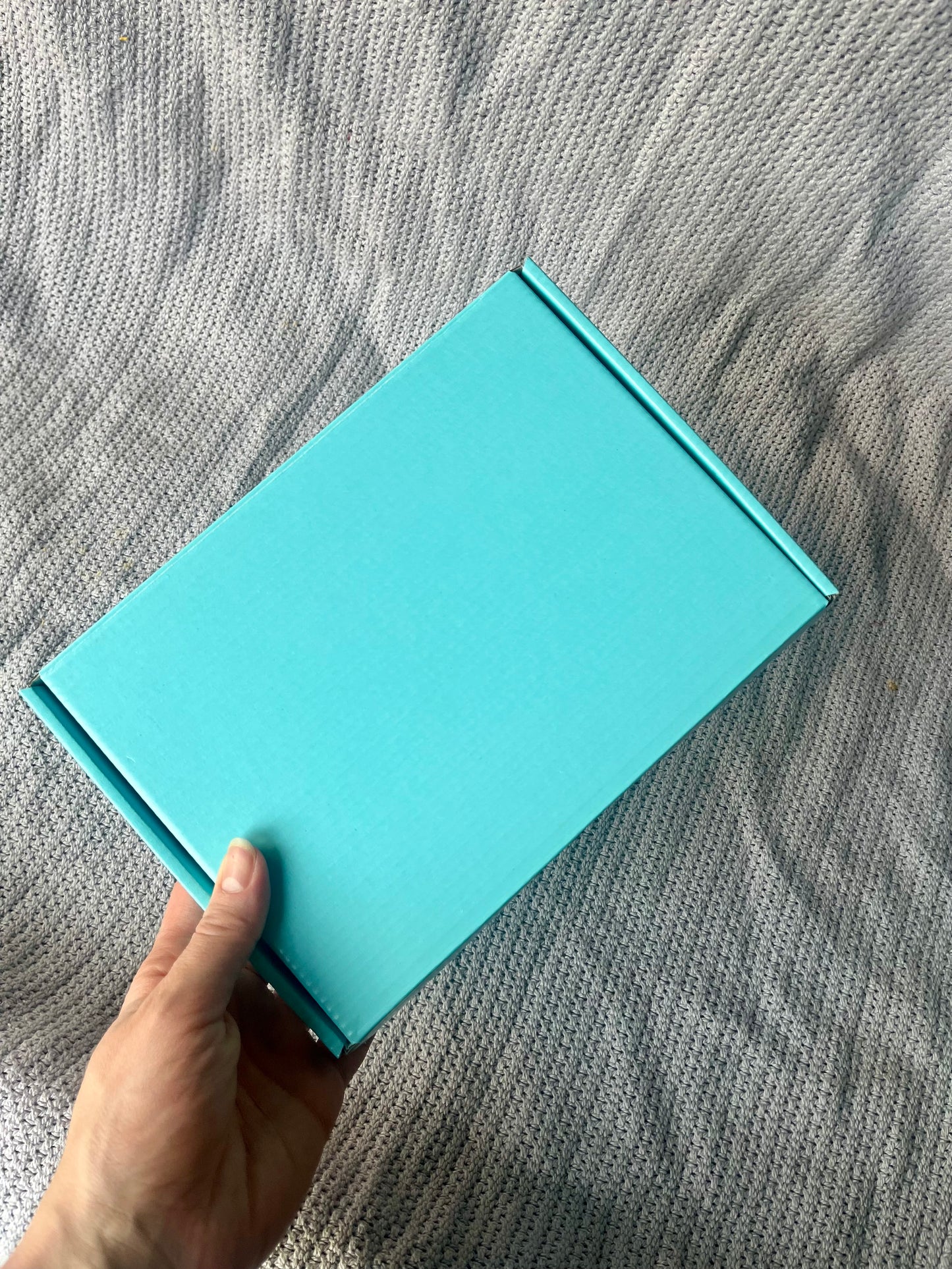 Hand holding a turquoise box on a textured gray surface