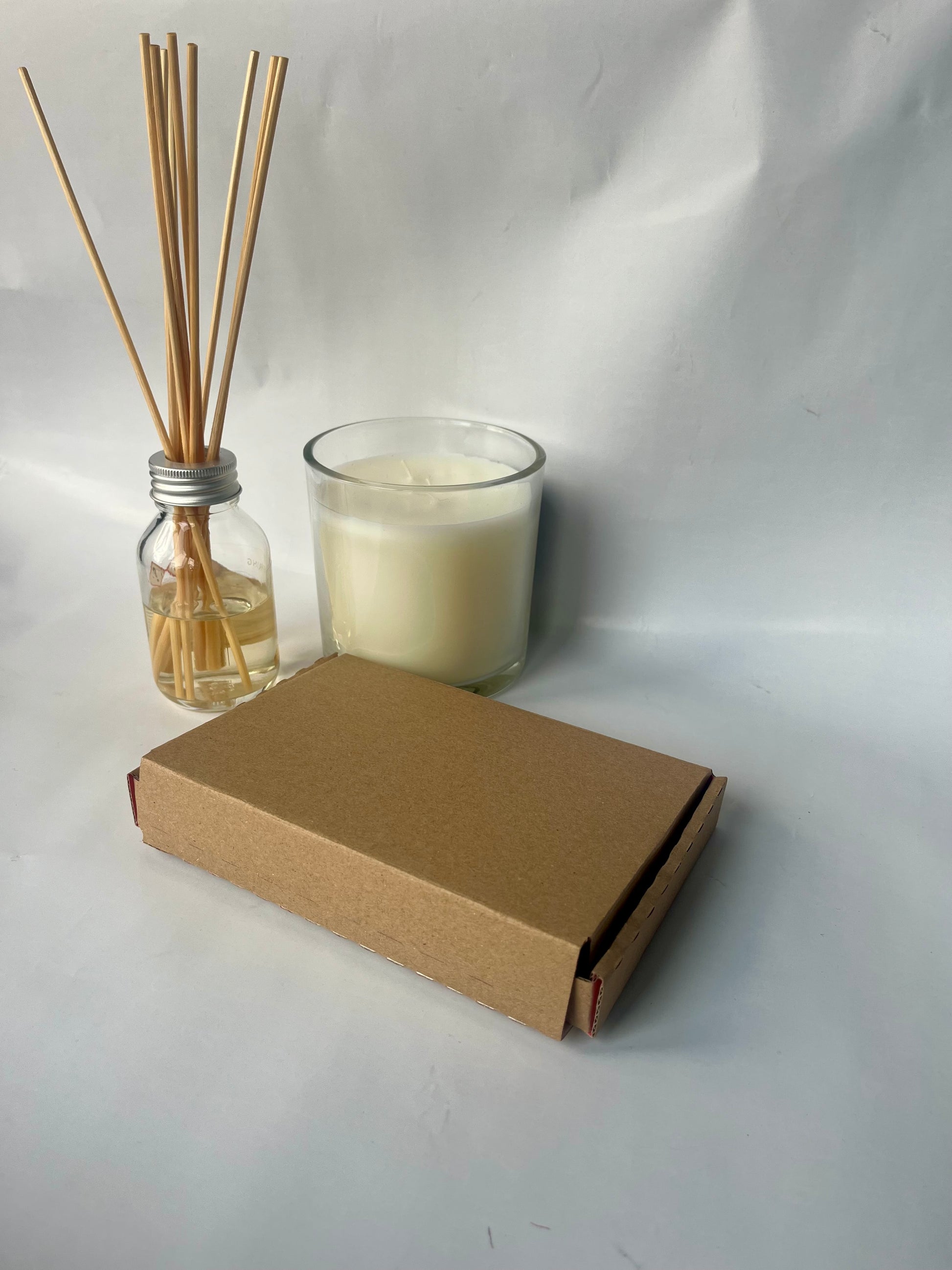 Candle, diffuser sticks, and cardboard box on a white background
