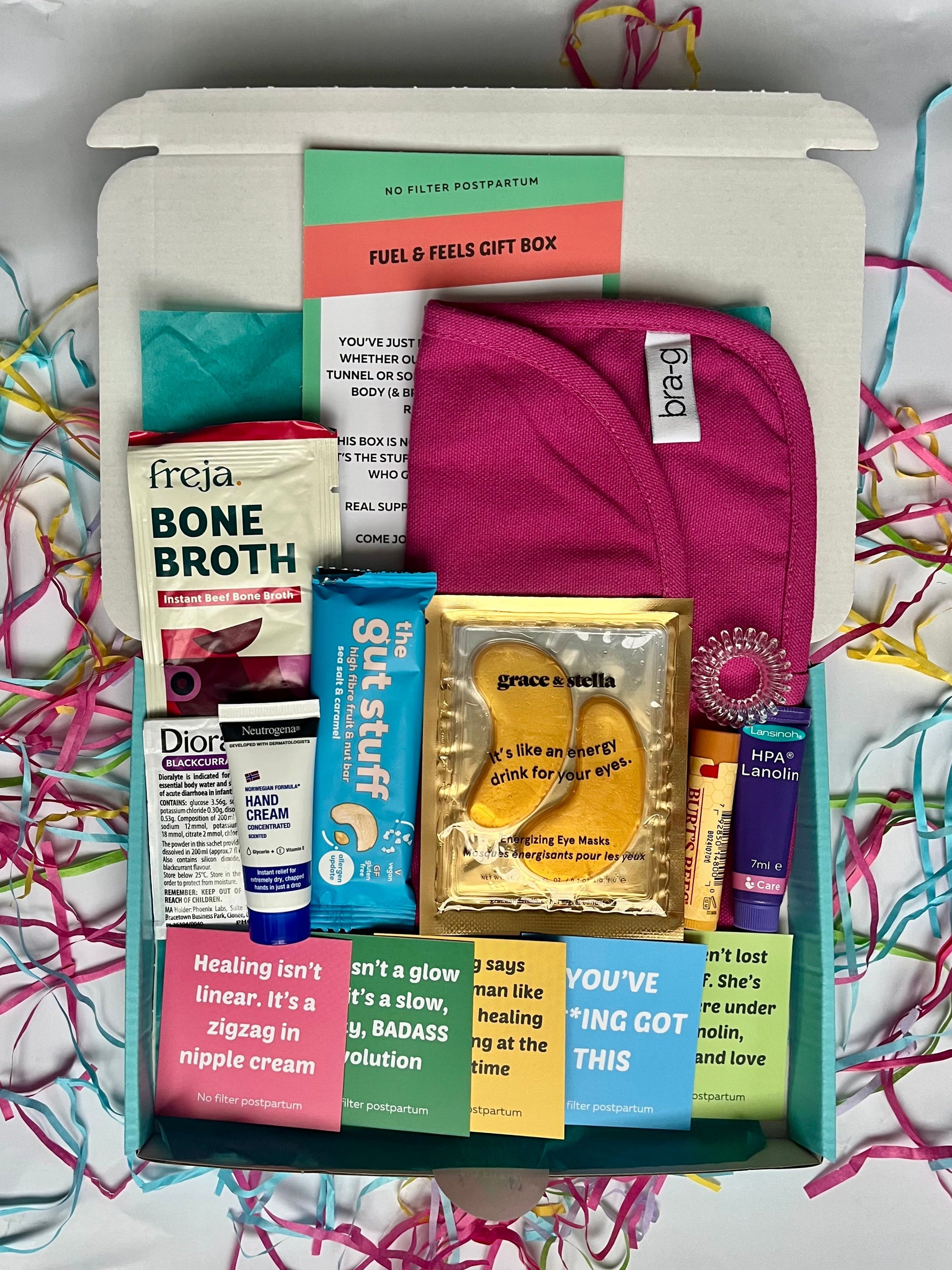 Gift box with various items including a pink towel, bone broth package, and other products on a colorful background.